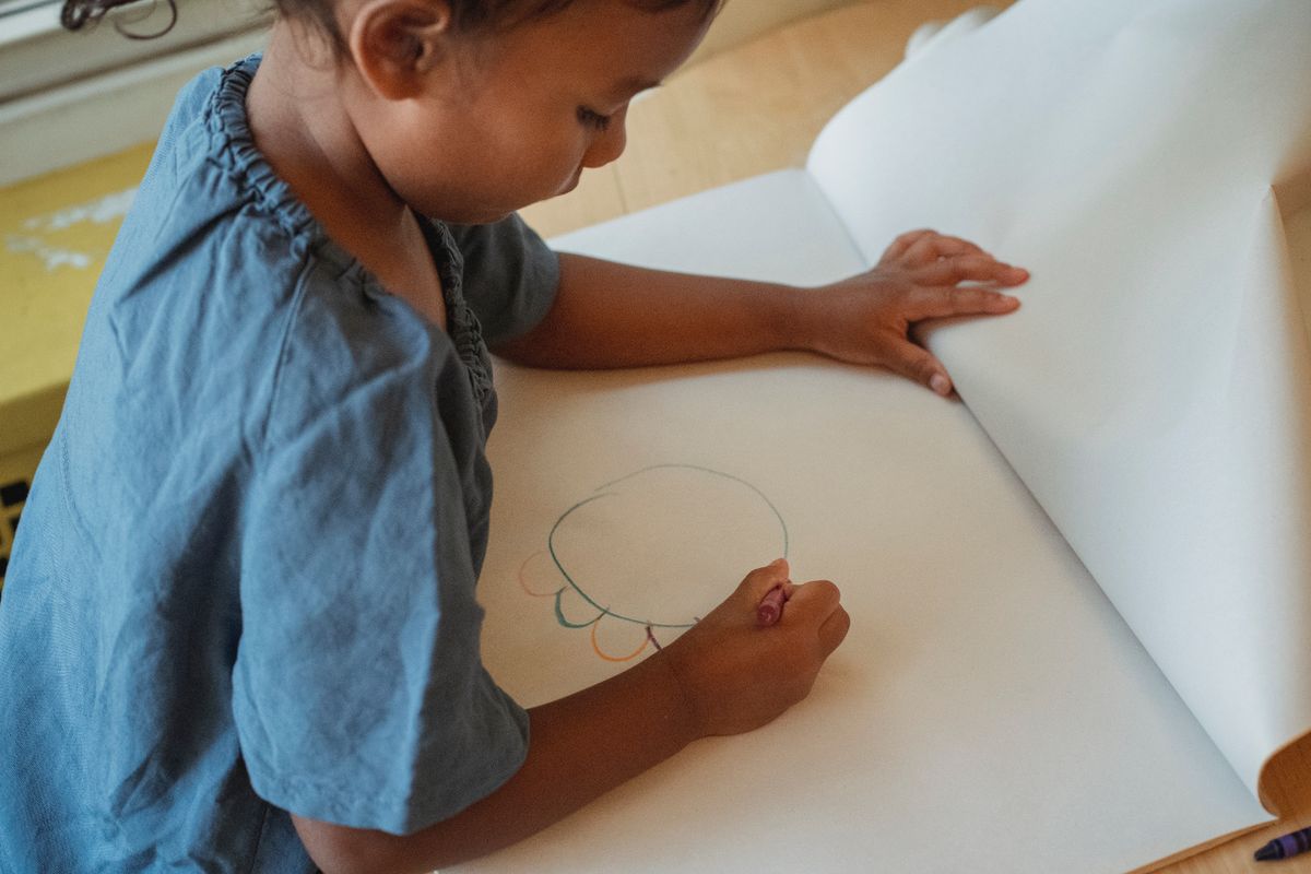 Little girl drawing at a wooden table with paper and colored pencils for a round owl