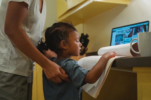 Unrecognizable ethnic woman working on netbook and helping little daughter with homework