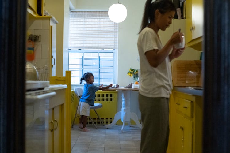 Asian Mother With Daughter Drinking Coffee In Kitchen