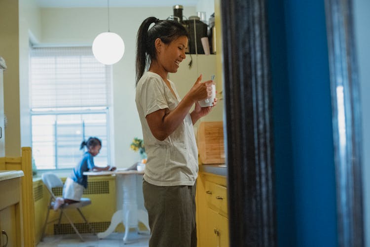 Cheerful Asian Mother With Cup Of Coffee In Kitchen With Daughter