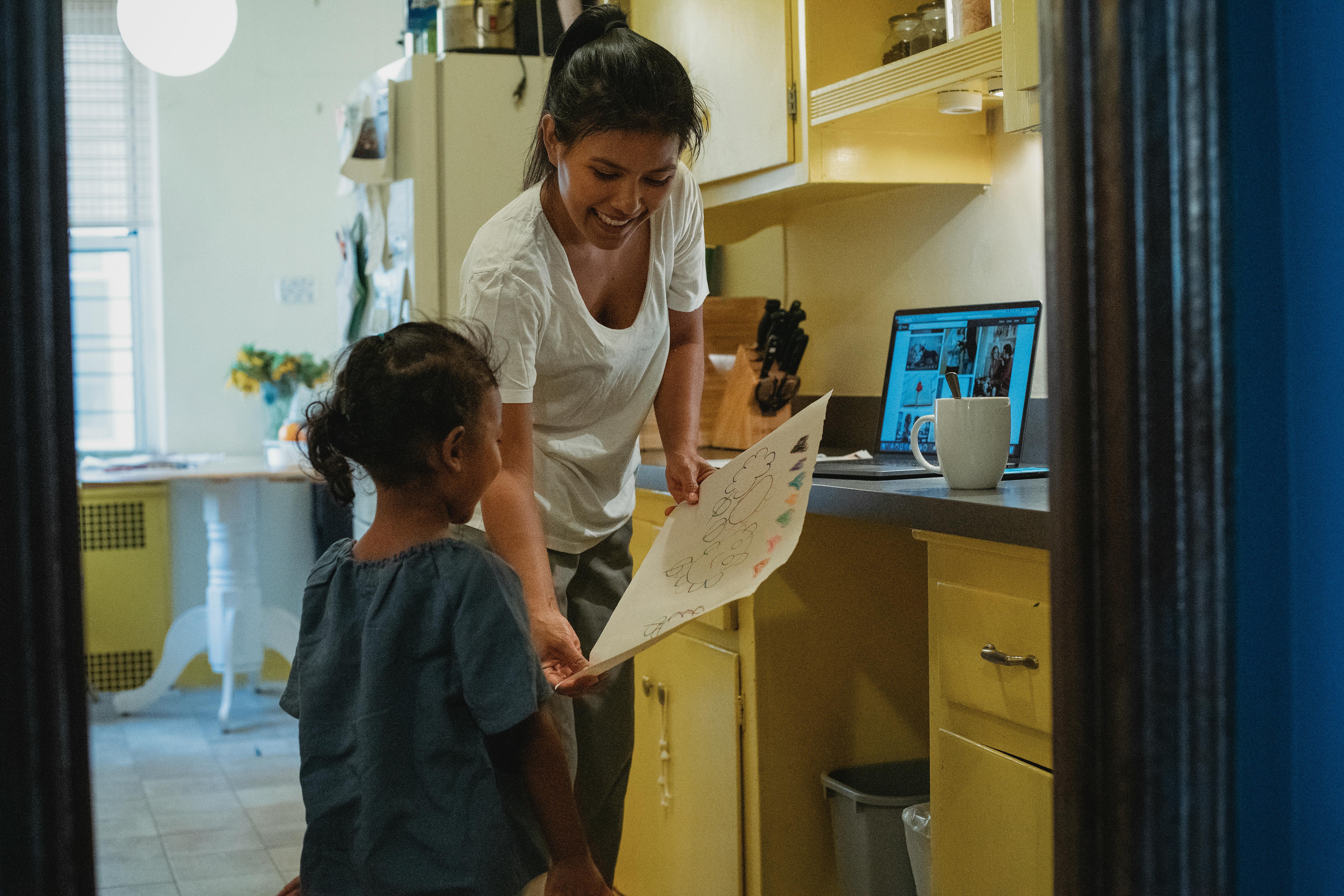 cheerful asian mother with drawing in kitchen