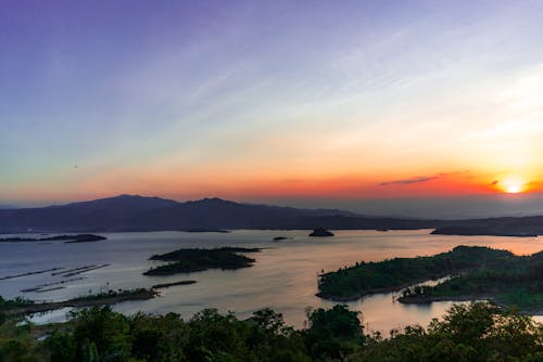 Picturesque seascape with green trees and hills against sundown sky