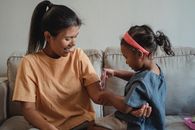 一位快乐的母亲和她的女儿在舒适的客厅里玩着玩具注射器扮演医生