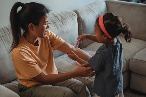 Free Side view of ethnic daughter making injection with fake syringe to Asian mother while playing game in living room during weekend Stock Photo