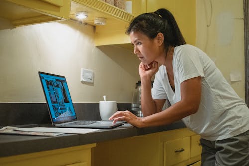 Free Focused Asian woman browsing laptop in kitchen Stock Photo