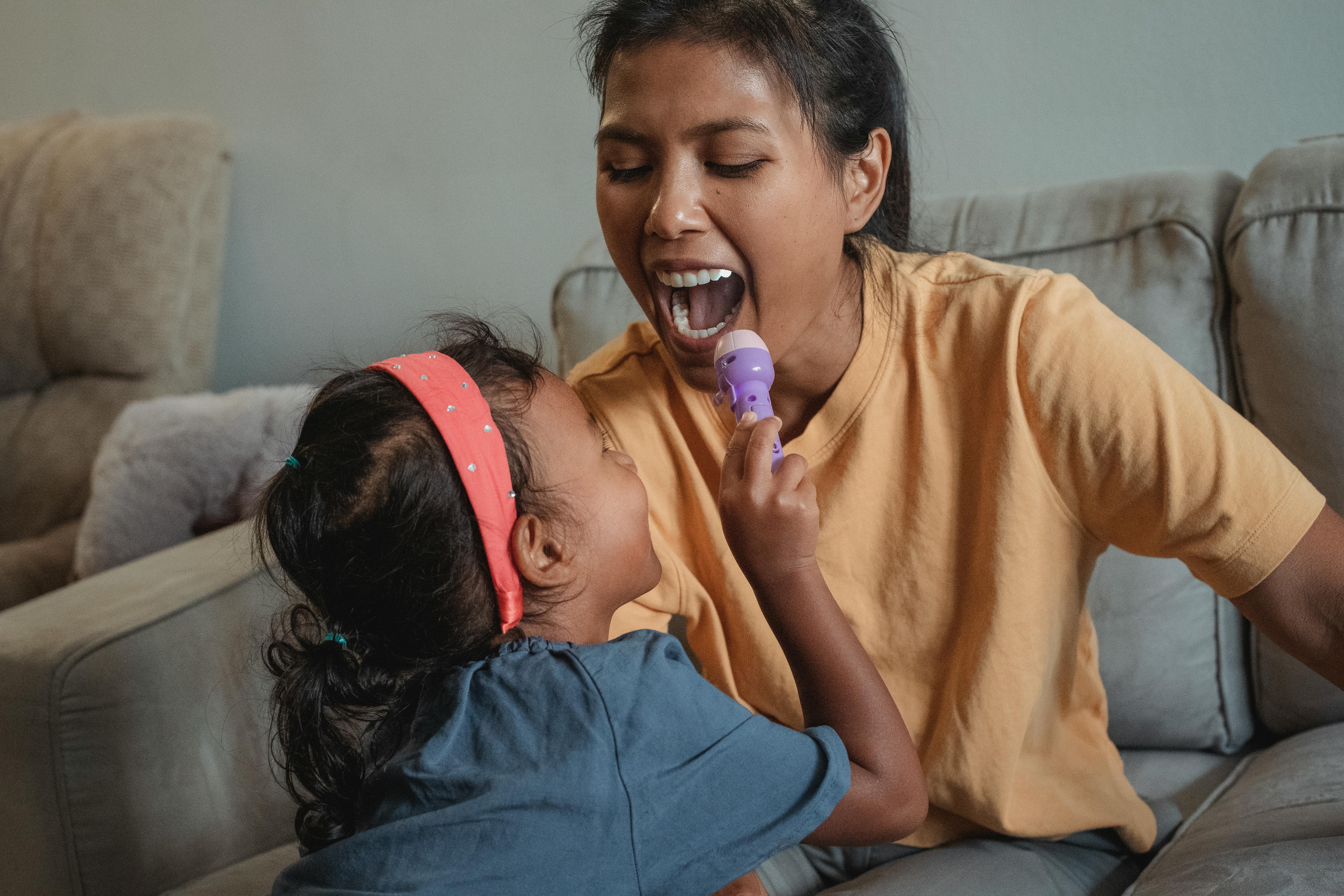happy ethnic mother with opened mouth playing doctor with daughter