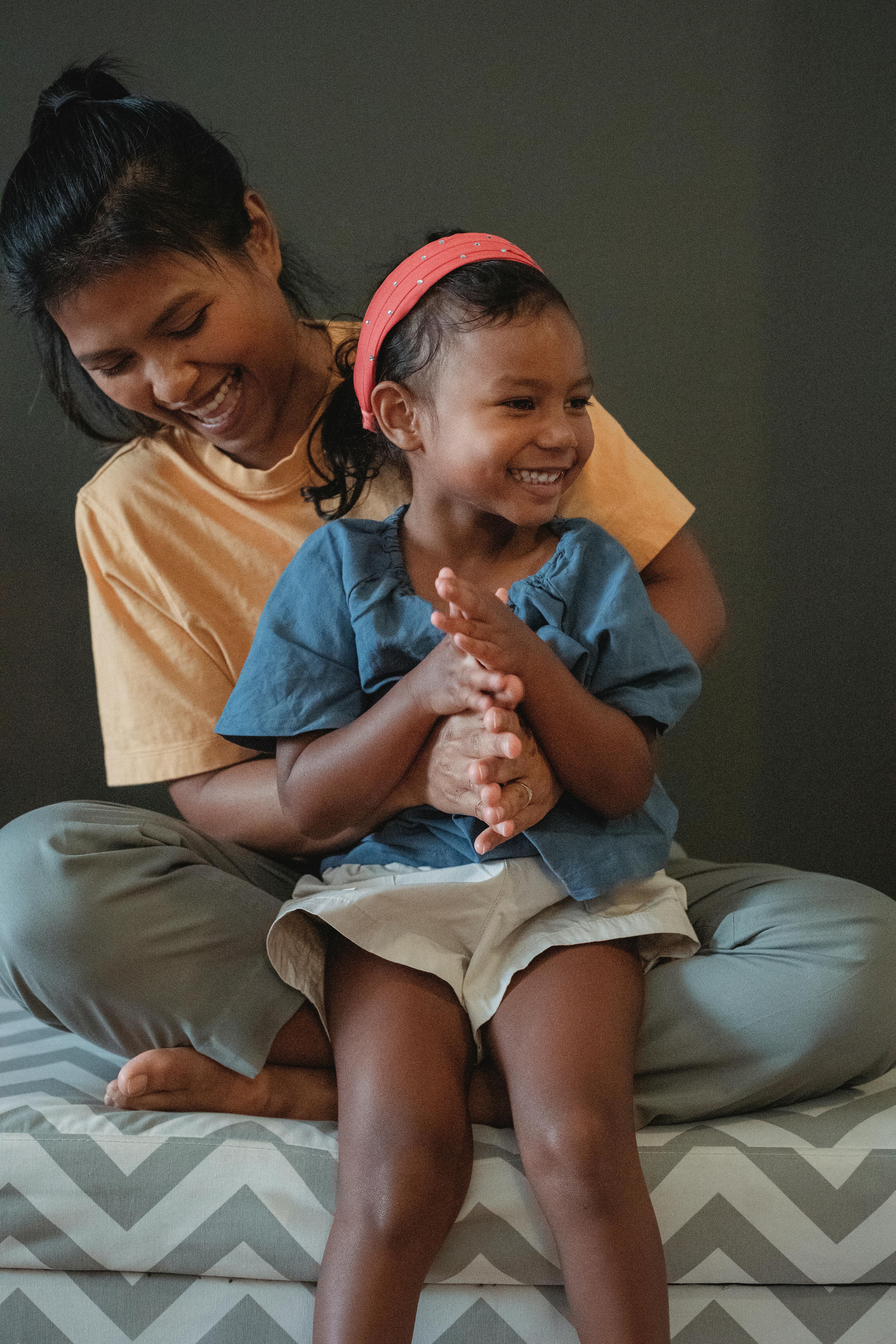 cheerful asian daughter sitting on crossed legs of mother