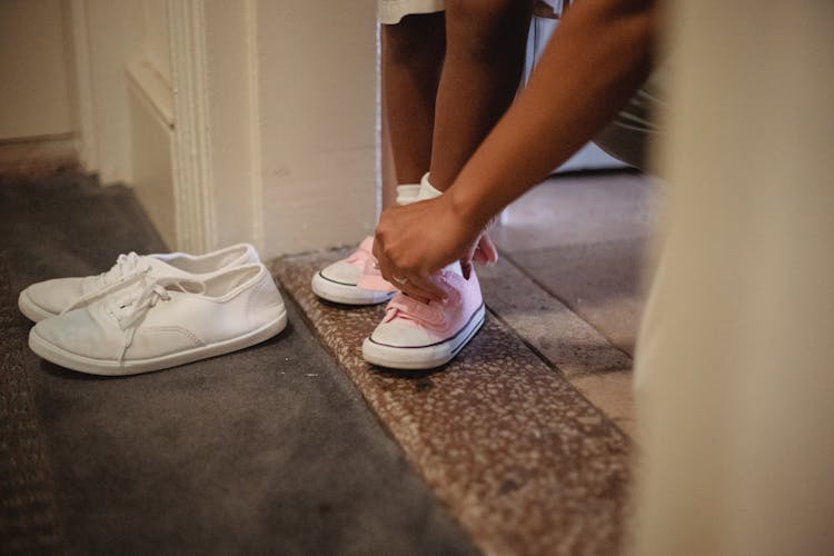 Crop Ethnic Woman Tying Shoes Of Anonymous Girl