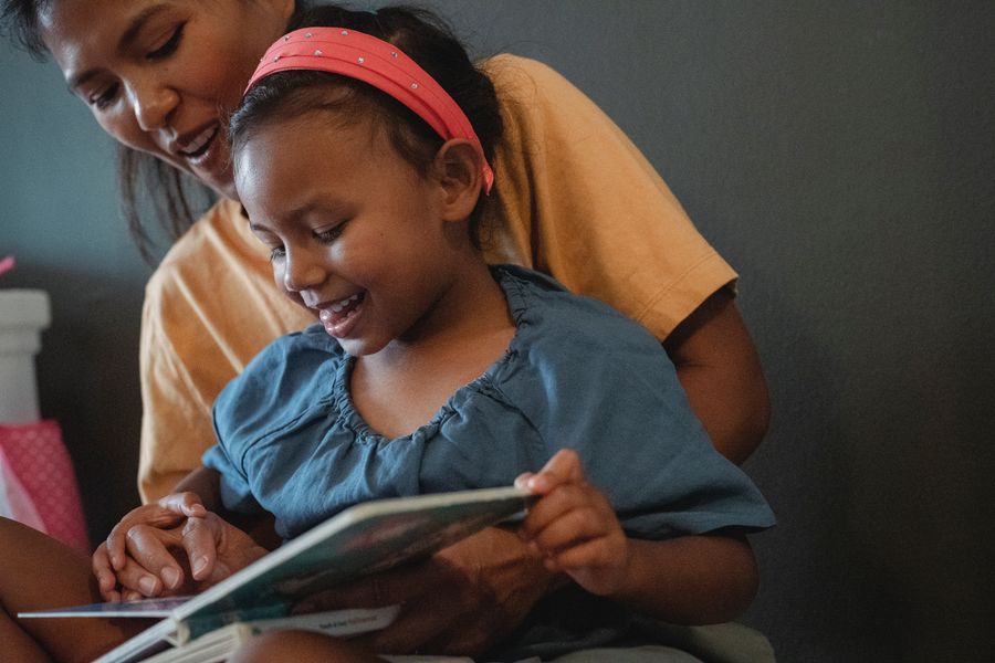 A parent and school-age child smiling while reading together
