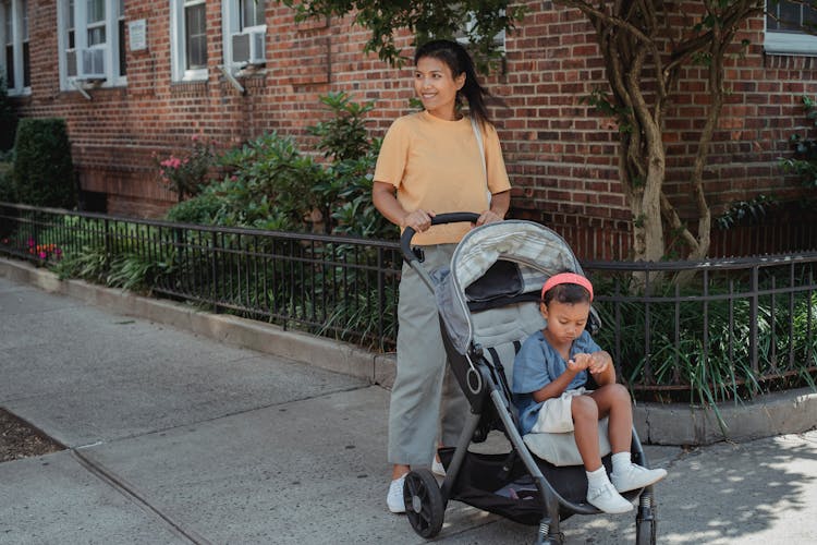 Happy Asian Mother With Cute Little Daughter On Baby Carriage