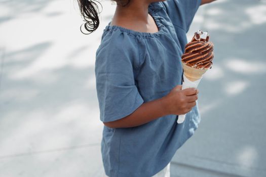 Crop anonymous ethnic girl in casual outfit with tasty sweet appetizing waffle ice cream cone on street in summer
