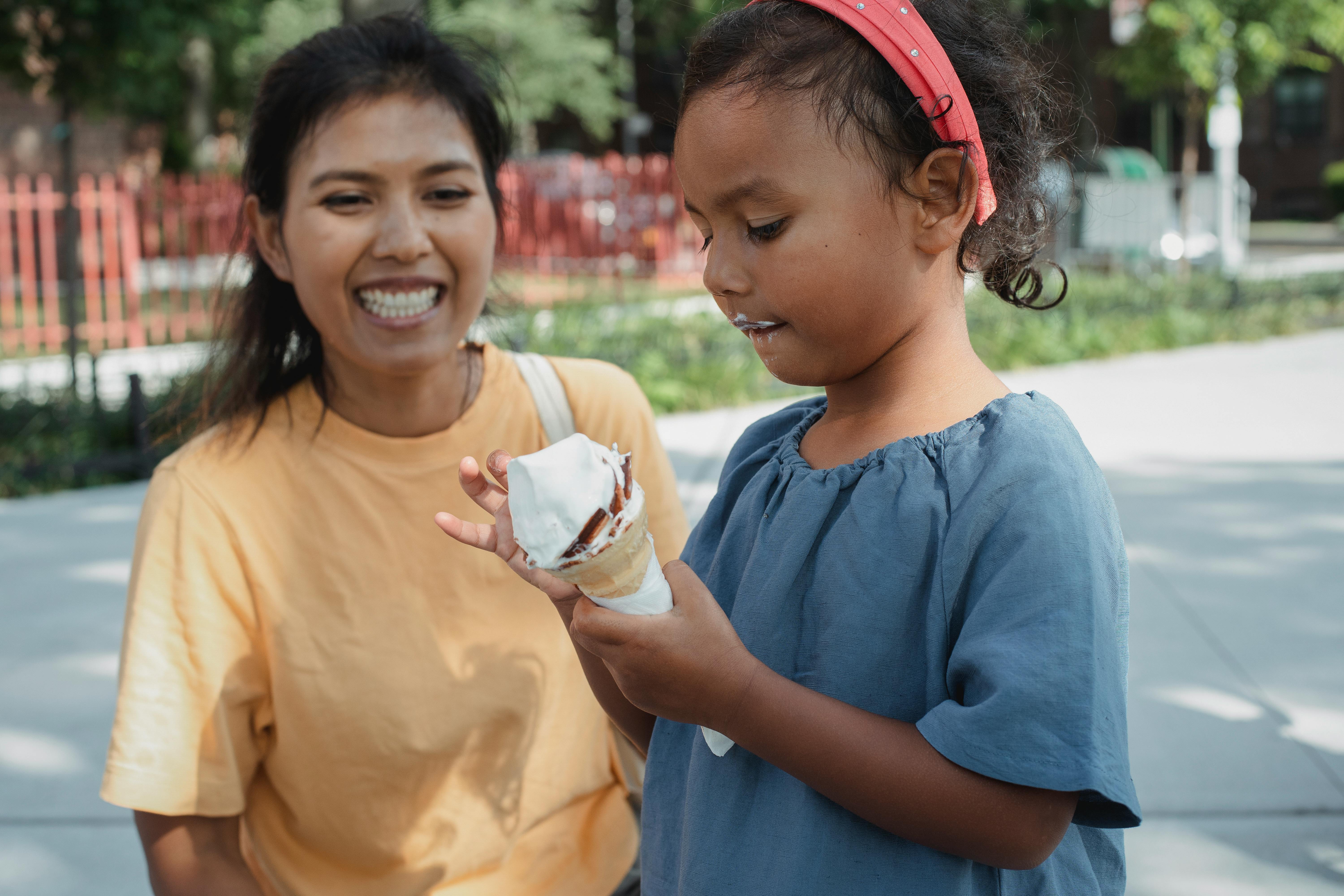 cheerful asian mother looking at daughter eating ice cream