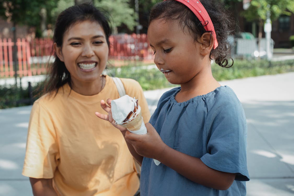 Cheerful Asian mother looking at daughter eating ice cream