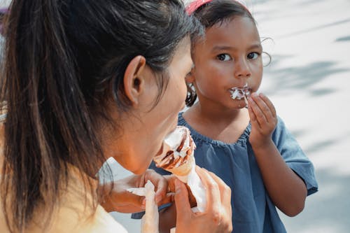Free Crop anonymous ethnic mother eating and sharing delicious sweet ice cream with adorable little daughter Stock Photo
