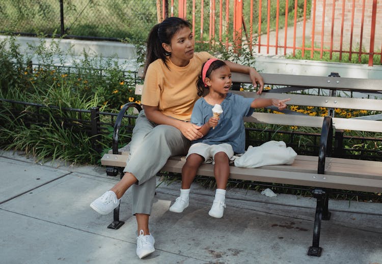 Asian Mother And Kid Sitting On Bench On Street In Sunny Day