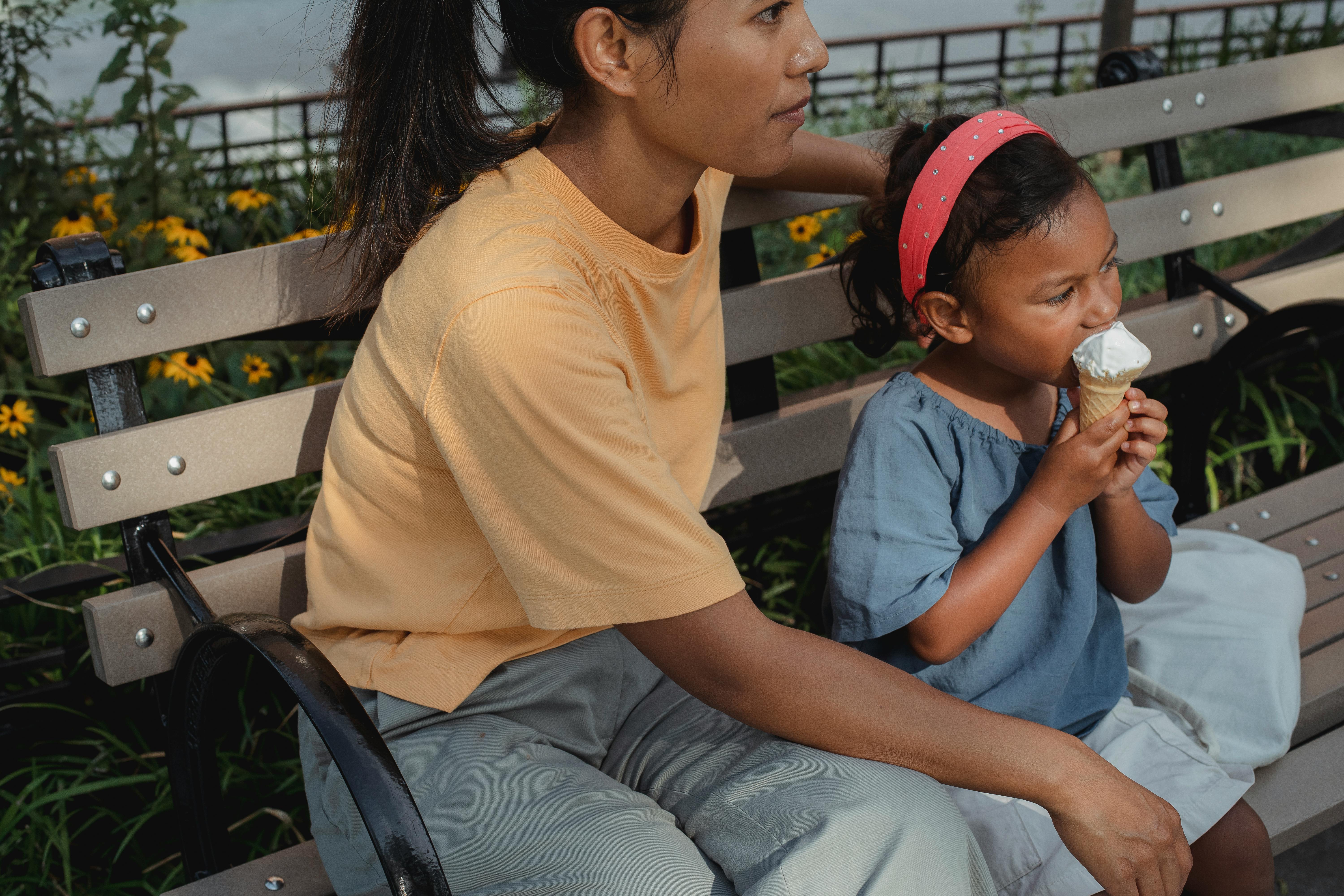 kid eating tasty ice cream and sitting on street bench with mother