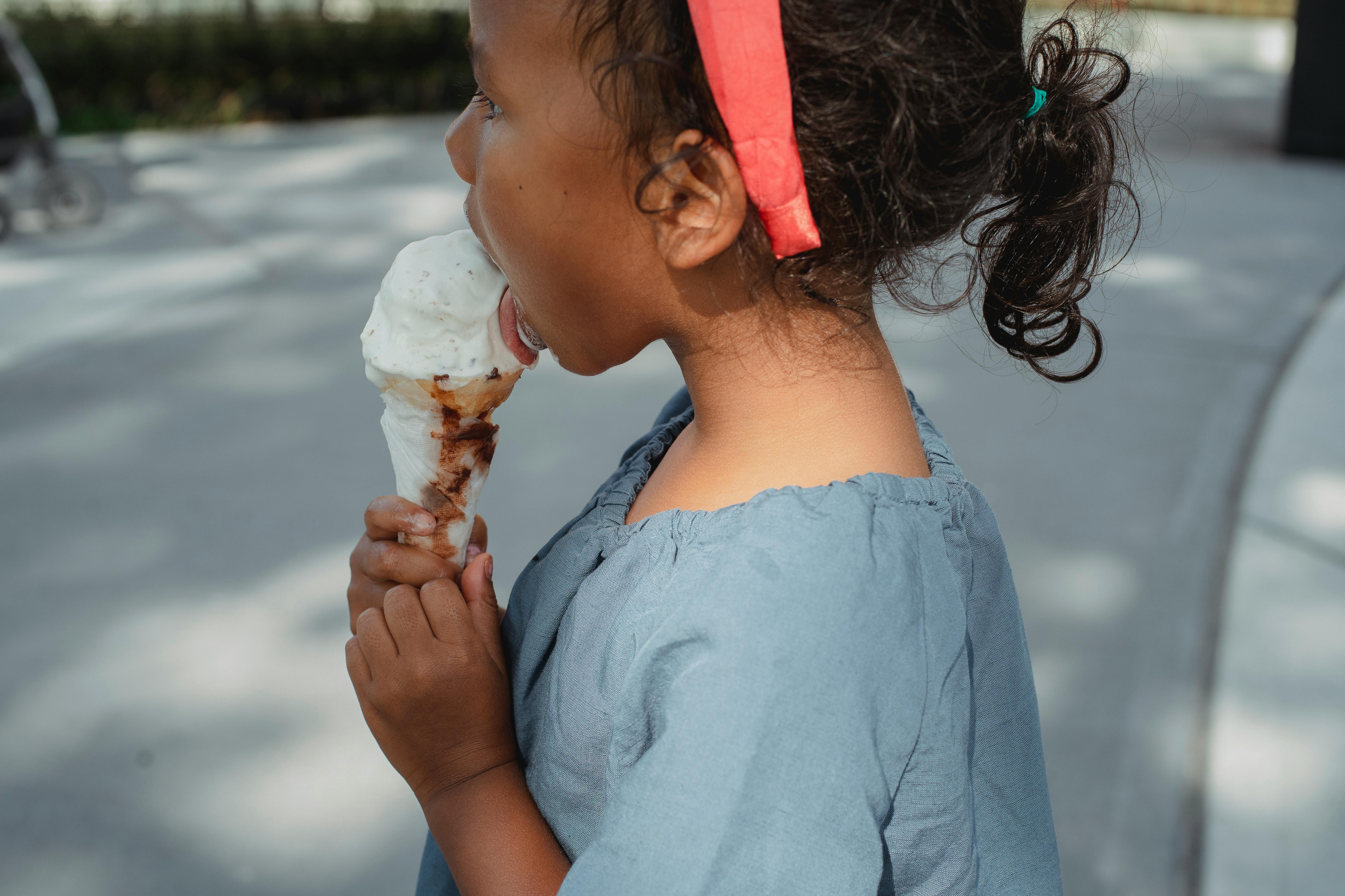 cheerful ethnic kid licking tasty ice cream on street