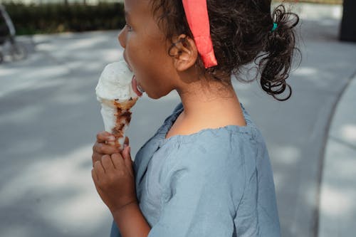 Side view of calm Asian girl with dark hair in casual outfit walking on street and licking delicious ice cream in summer time