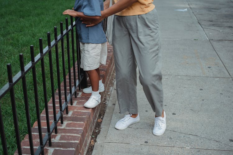 Crop Mother And Daughter Standing Near Metal Fence On Street