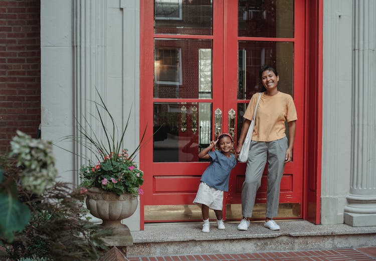 Cheerful Asian Mother And Daughter Standing Near Entrance Of House