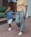 Happy Asian daughter holding hands of crop mother and showing grimace and peace sign while walking on tiled walkway together