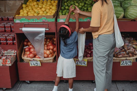 A mother and daughter selecting fruits and vegetables at an outdoor market.