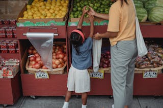 Ethnic woman choosing fruits with daughter in market