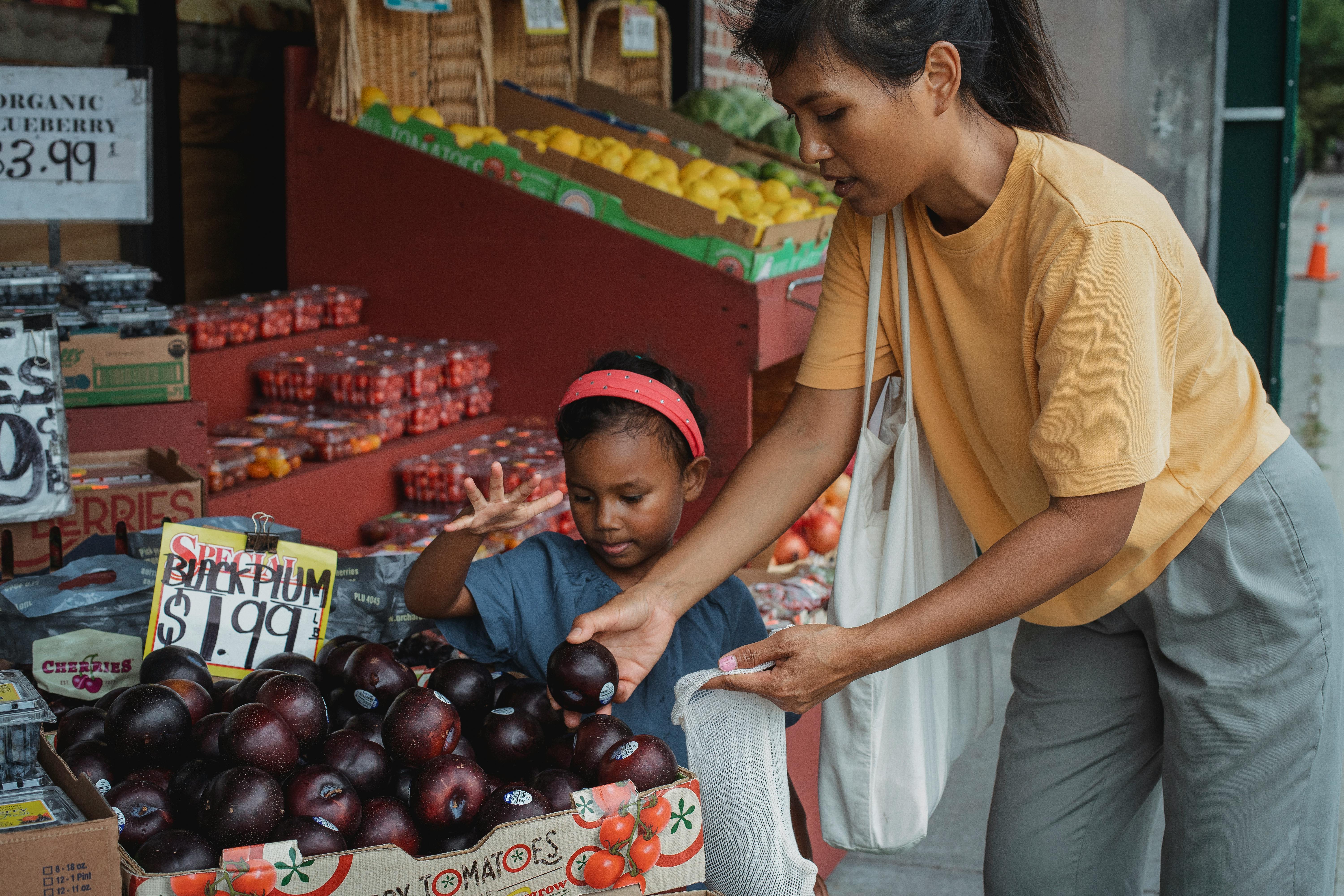 ethnic customer choosing fruits with daughter at market