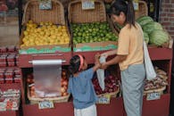 亚洲女孩与母亲在市场购物时，从盒子里挑选成熟的酸橙放入环保袋的后视图