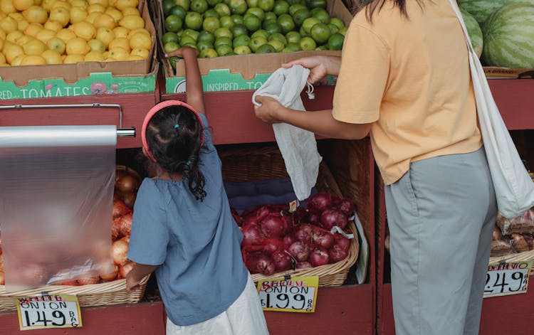 Ethnic Woman With Daughter Picking Limes In Market