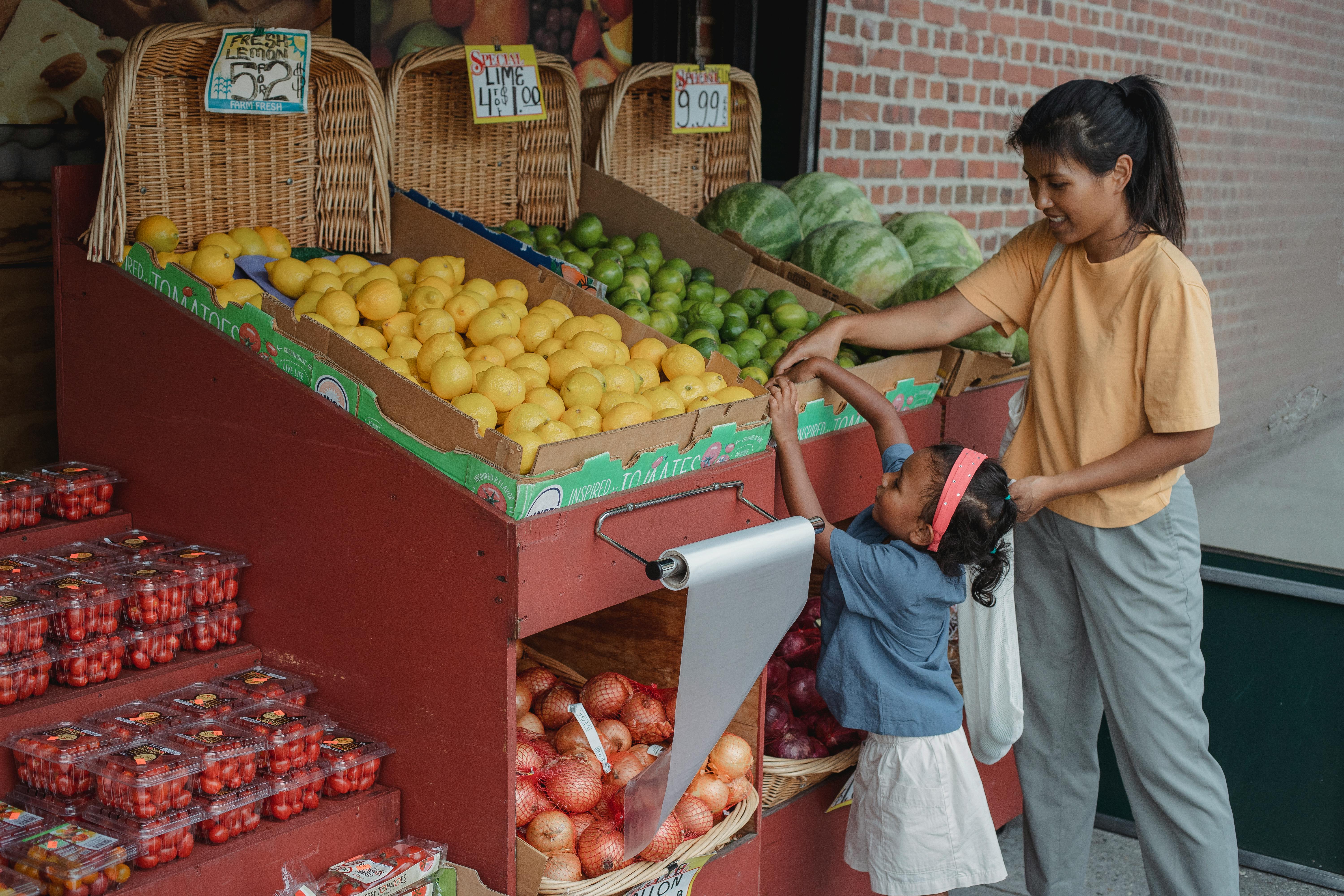 small ethnic girl taking fruits from box with mother