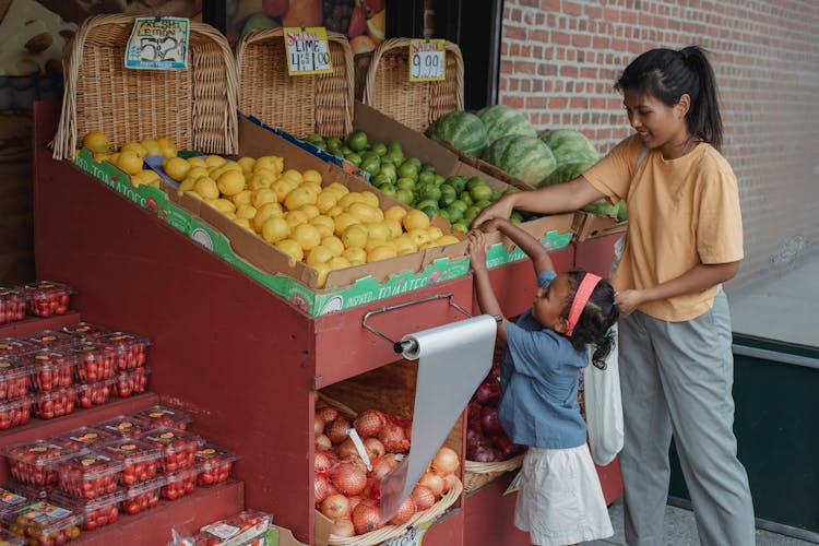 Small Ethnic Girl Taking Fruits From Box With Mother