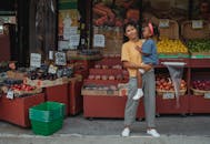 母女俩在当地热闹的户外市场愉快地探索购物，那里摆满了五颜六色的水果和蔬菜