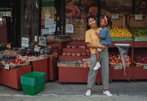 母女俩在当地热闹的户外市场愉快地探索购物，那里摆满了五颜六色的水果和蔬菜