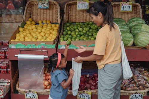 Free Back view Asian woman with daughter wearing casual outfits standing near local street market stall and choosing fruits Stock Photo