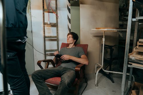 Man in Red Polo Shirt and Blue Denim Jeans Sitting on Brown Wooden Armchair