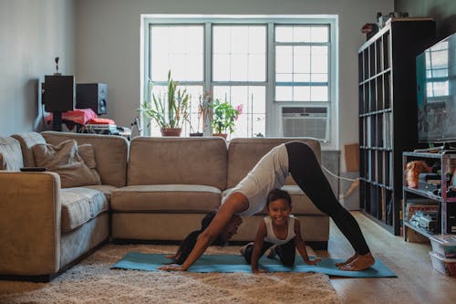 Cheerful Asian girl sitting under mother practicing yoga at home