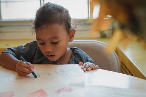 Focused Asian girl drawing with crayons at home