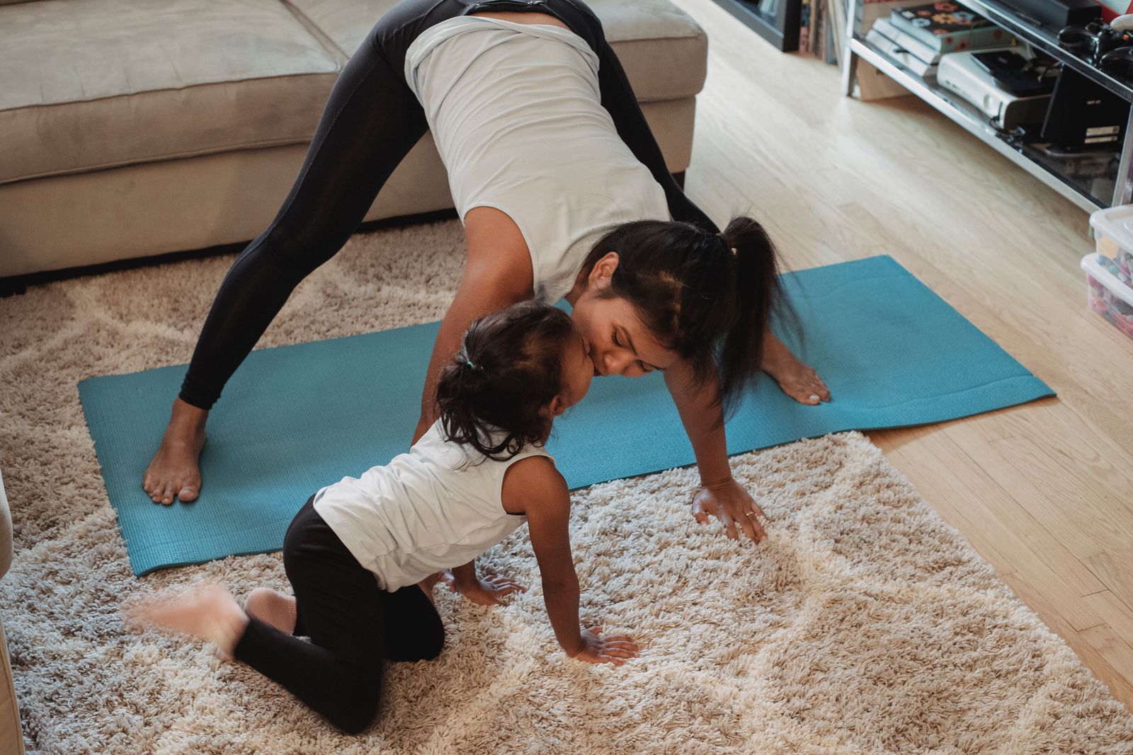 Mother practicing downward facing dog pose while bonding with her baby during a postnatal yoga session at home