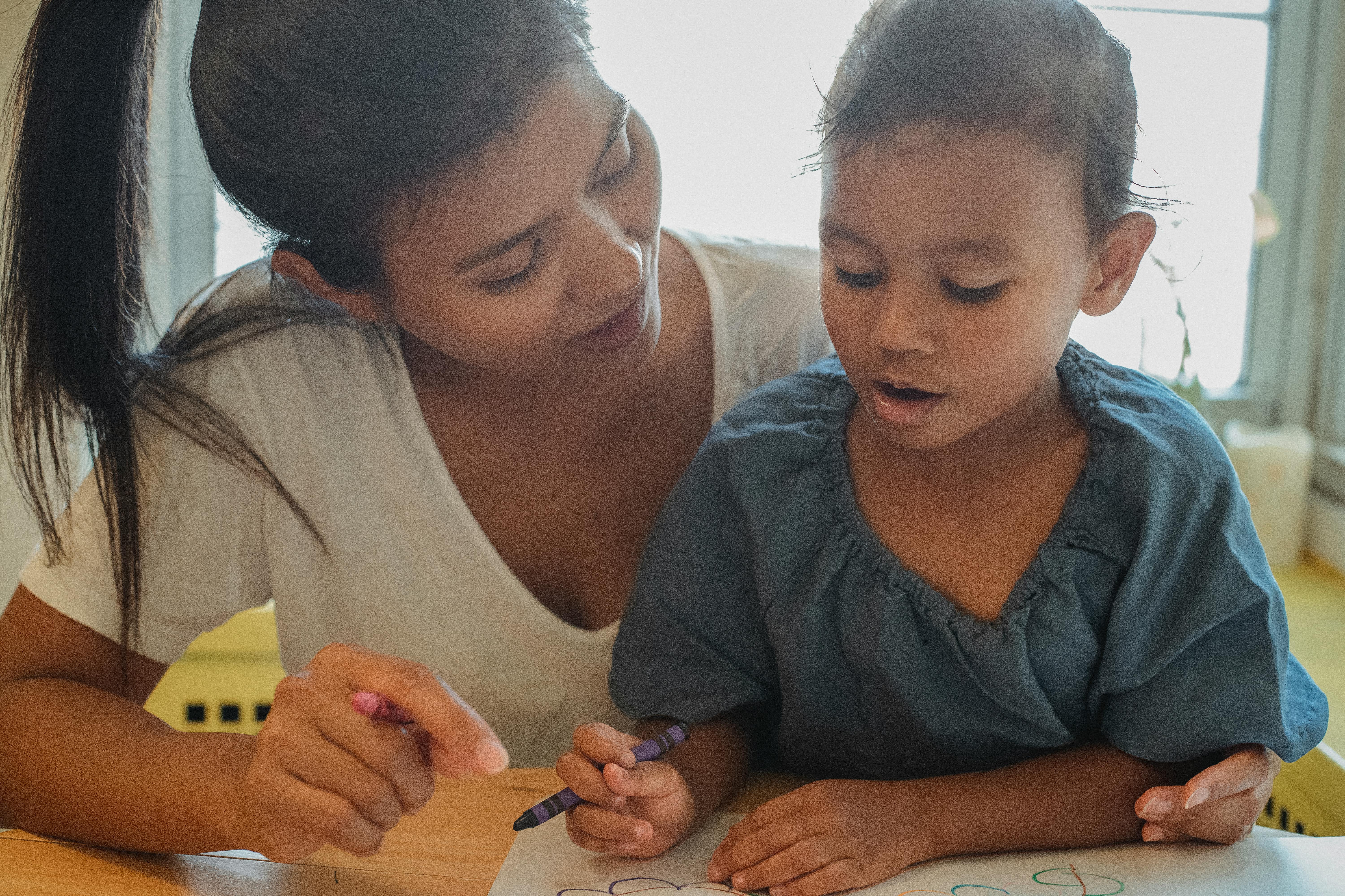crop ethnic woman and daughter drawing together at home