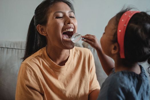 Crop Asian mother and daughter playing dentist game together
