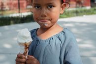 Crop adorable little Asian girl in casual clothes eating ice cream and looking at camera