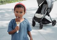 Cute Asian little girl in casual outfit eating yummy chocolate ice cream cone and looking away