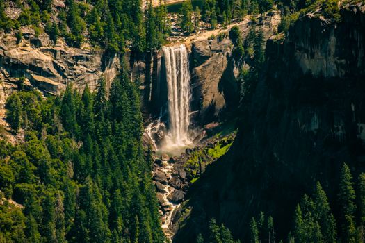Stunning waterfall cascading down a cliff in Yosemite Valley, surrounded by lush greenery.