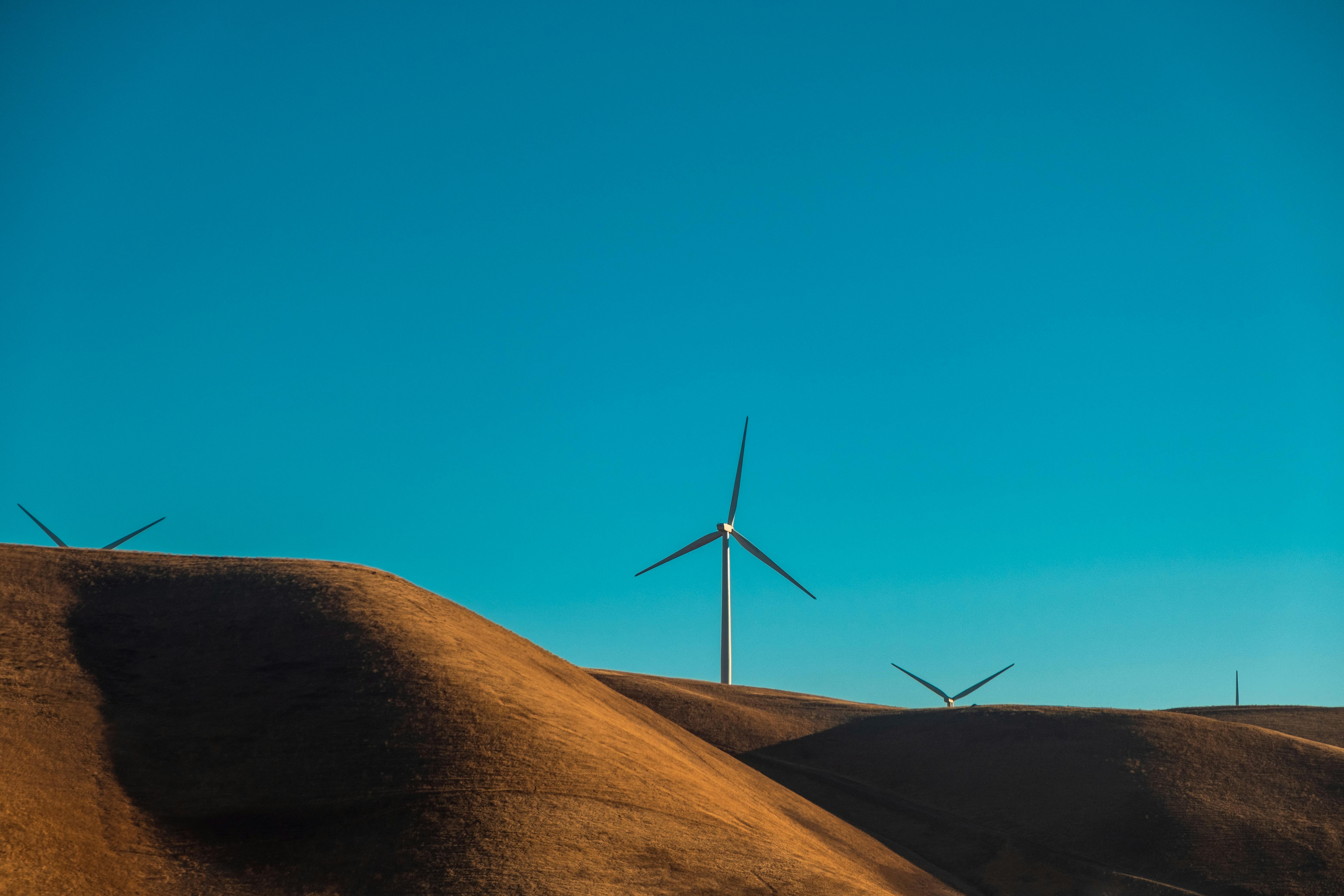 Wind turbines on sandy dunes under a clear blue sky, showcasing renewable energy in a desert environment.