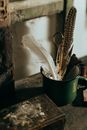 木桌上放着一个复古马克杯，里面装满了羽毛和旧工具，场景质朴