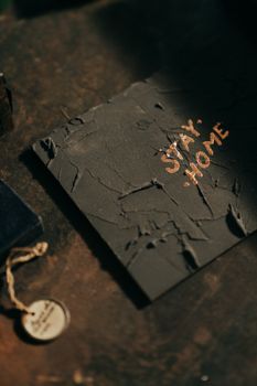 A textured slate sheet with 'Stay Home' message placed on a rustic dark surface, evoking a vintage gothic atmosphere.