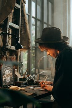 一个男人戴着帽子，在老式桌子上写字，周围摆着各式各样的物件，光线柔和