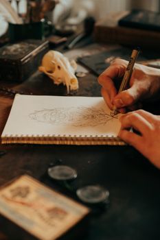 一位艺术家在老式书桌上，正对着记事本素描，周围散落着创意物品和头骨