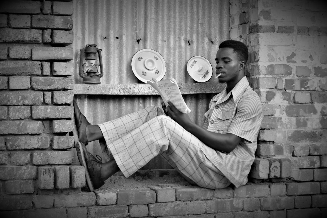 black and white photo of a man reading and smoking in a relaxed pose a